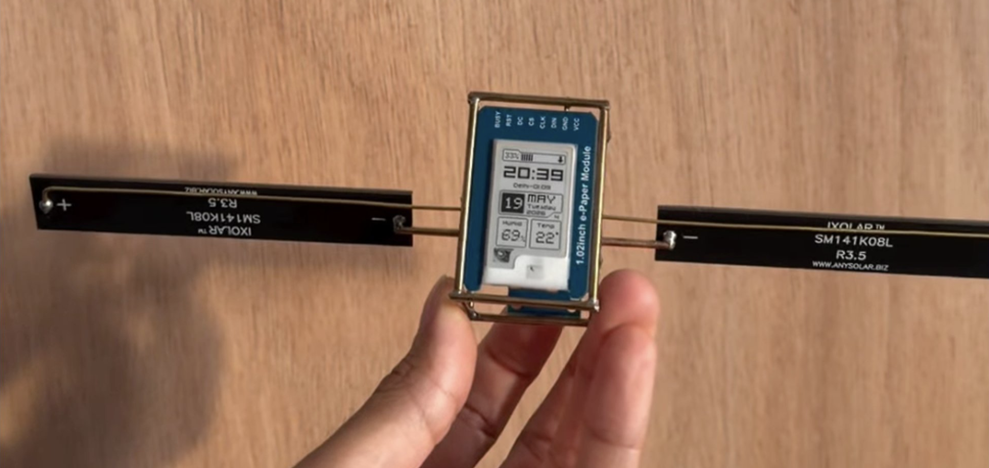 CLOCK-SAT V1 by Maxime Loiseau: a 1.02-inch e-paper module in a brass frame with solar-cell wings